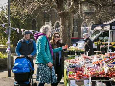 A group of people at a market stall full of fresh fruit and veg. 