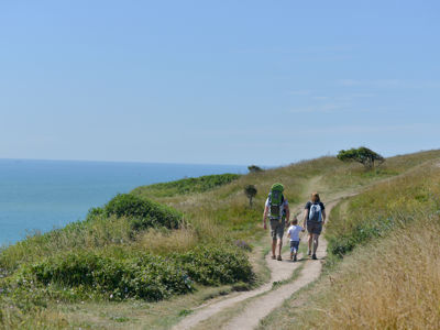 Two adults holding hands with a small child walking on the White Cliffs of Dover - blue sea and sky.