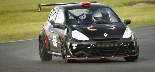 Photo of a black car driven by a racing driver going round a race track.