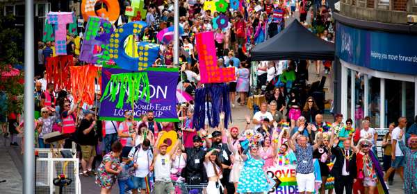 A colourful crowd walking through Dover streets with rainbow banners