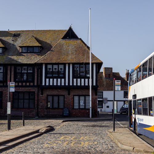 A red, yellow, blue and white Stagecoach bus at a bus stop outside Sandwich Guildhall.