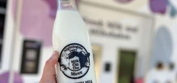 A full milk bottle being held up in front of a mobile vending machine.