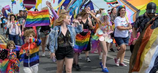A crowd of people walking along waving rainbow flags.