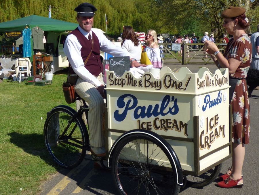 A man riding an ice-cream bicycle and a woman in vintage clothing