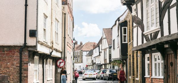 A street of medieval buildings in Sandwich a few people and cars in the distance.