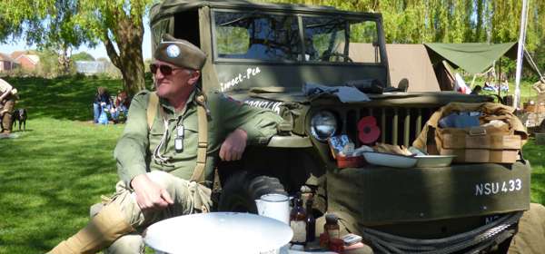 A man in vintage army gear sitting next to an old army jeep.