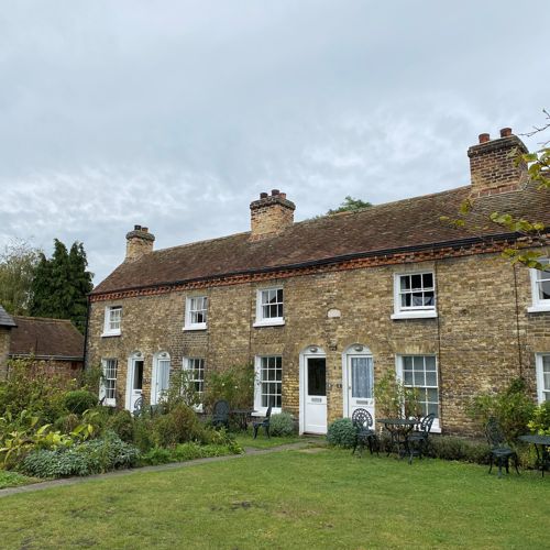 A row of sandy brick terraced cottages with gardens in front.