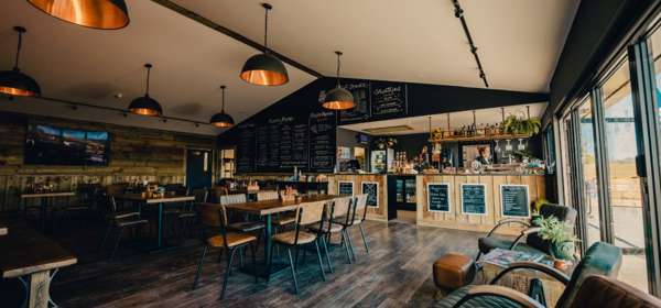 Interior of Whitemills kitchen with wooden floors and walls. Long wooden tables with seating for 6 people