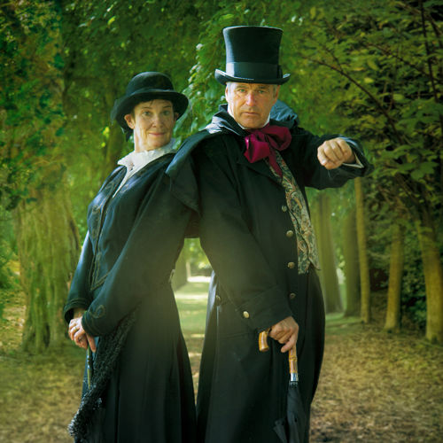 A couple dressed in black Victorian clothing in a spooky woodland scene